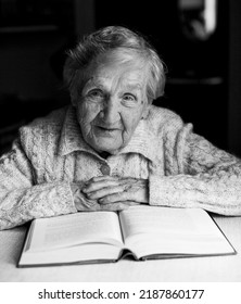 A Portrait Of An Old Lady Reading A Book In Her Own Home. Black-and-white Photo. 