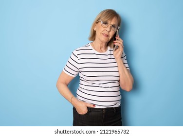 Portrait Of Old Lady Wearing Striped T-shirt Using Mobile Phone Standing Isolated Over Blue Background. Technology Concept.