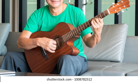 Portrait Of Old Man With Acoustic Guitar With Happiness Retirement, On Sofa In Room, Concept Music Therapy.