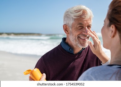 Portrait of old man looking at his mature wife applying sunscreen on nose. Senior husband enjoying vacation with woman while applying sunscreen on face at beach. Middle aged retired couple at sea. - Powered by Shutterstock