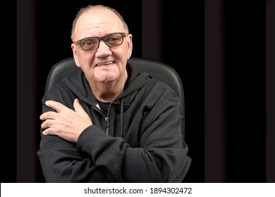 Portrait Old Man With Smirk Sitting In Armchair With Crossed Arms On Black Background