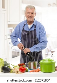 Portrait Of Old Man Standing At Kitchen And Cooking Healthy Food For Dinner. 