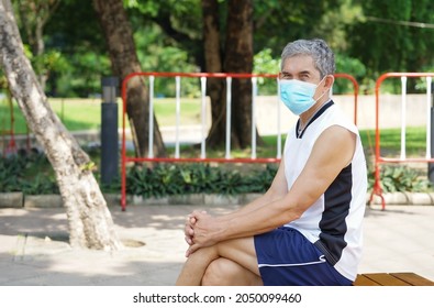 Portrait An Old Man Wearing Protective Face Mask, Sitting Social Distancing In The Park After Exercise, Concept New Normal Life During Coronavirus Is Spreading                               