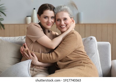 Portrait of old mother and mature daughter hugging at home. Happy senior mom and adult daughter embracing with love on sofa