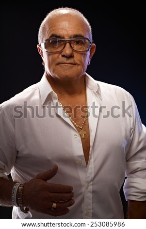 Portrait of old playboy in white shirt and lots of gold jewels.