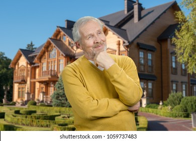 Portrait Of Old Thoughtful Grandfather. Rich Senior Man Thinking On His Big House Background.