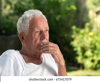 Portrait of old thoughtful man in park with green background. Senior care and depression concept