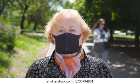 Portrait Of Old Woman With Black Face Mask Stands At City Street. Grandmother Wears Protective Mask From Virus COVID-19 Outdoor. Concept Of Health And Safety Life From Coronavirus Pandemic. Close Up