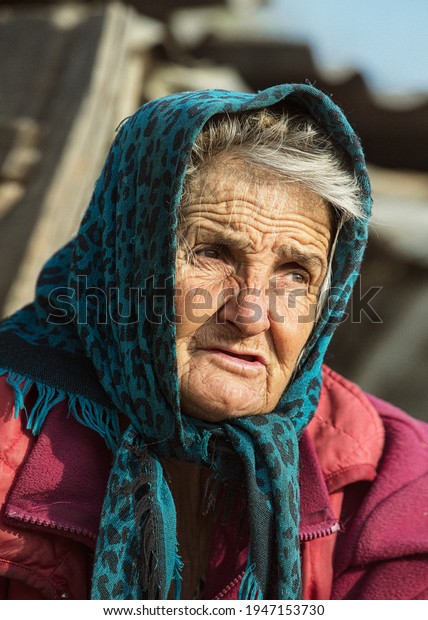 Portrait of an old woman in a blue\
headscarf. The face of the old woman is wrinkled with a deep look.\
Image with selective focus and noise effect,\
toning