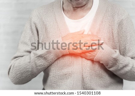 portrait of old woman holding breast because of heart infarction on gray background