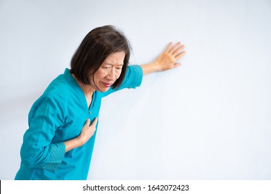 Portrait Of Older Asian Woman With Unhappy Face And Blue Blouse Getting Chest Pain, White Background