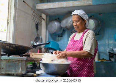 Portrait of older Asian woman wearing chef hat and pink apron cooking Thai food in kitchen at home. 
Grandmother  preparing  rice vermicelli for made  Crispy Noodles - Powered by Shutterstock