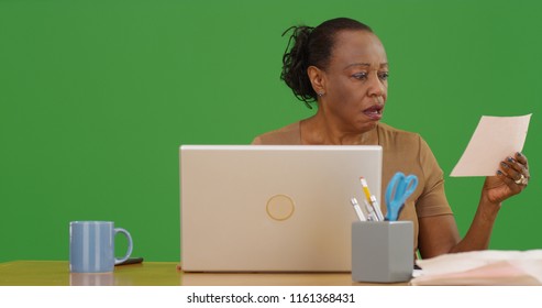 Portrait Of An Older Black Woman Using Computer To Pay Bills On Green Screen