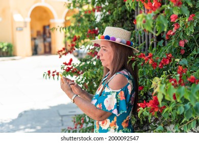 Portrait Of An Older Hispanic Woman Checking Her Cell Phone In The Open Air.