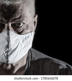 Portrait Of An Older Man With Gray Hair. He Is Wearing A Medical Mask. The Background Is Black.