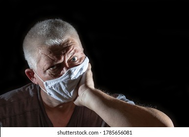 Portrait Of An Older Man With Gray Hair. He Is Wearing A Medical Mask. The Background Is Black.