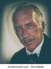 Portrait Of An Older White Man In Formal Dress Tuxedo, Slicked Back Hair And Pencil Mustache, Looking At Viewer With Old Fashioned Vintage Finish.