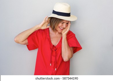 Portrait Of Older Woman Laughing With Hat Against Gray Wall