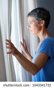 Portrait Of Older Woman Opening Curtains And Looking Out Window