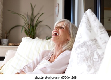 Portrait Of Older Woman Sitting On Sofa At Home And Laughing 