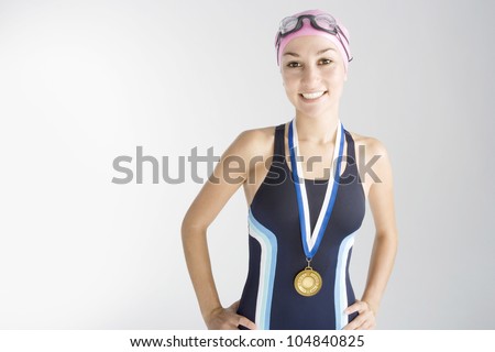 Portrait of an olympic swimmer wearing a gold medal and smiling at the camera.