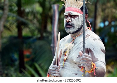 Portrait of one Aboriginal Australian adult male warrior, holding Aboriginal martial art weapons looking at camera, during Aboriginal cultural show in the tropical far north of Queensland, Australia.