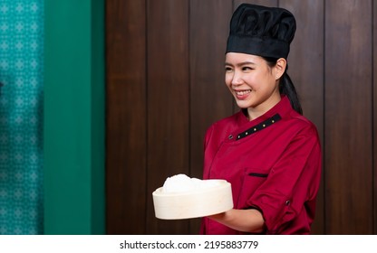 Portrait One Beautiful Traditional Professional Chinese Chef Wearing Red Uniform, Hat, Happily Smiling, Presenting Basket Of Food For Advertisement. Restaurant, Food, Hotel Concept