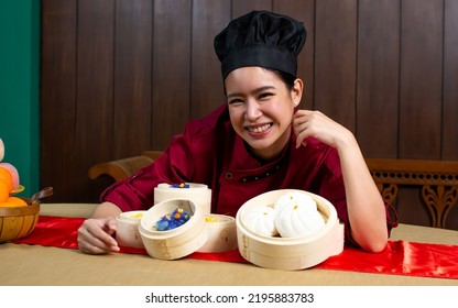 Portrait One Beautiful Traditional Professional Chinese Chef Wearing Red Uniform, Hat, Happily Smiling, Presenting Basket Of Food For Advertisement. Restaurant, Food, Hotel Concept