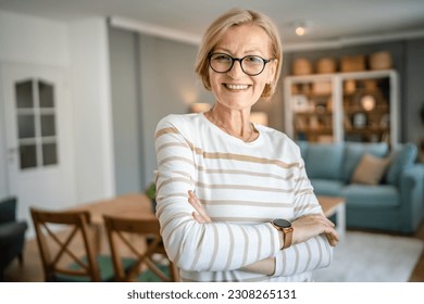 Portrait of one mature blonde caucasian woman with eyeglasses at home happy smile looking to the camera confident wear sweater in bright room copy space - Powered by Shutterstock