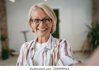 Portrait of one mature blonde caucasian woman with eyeglasses at home happy smile looking to the camera confident wear sweater in bright room user generated content self portrait selfie ugc copy space - Powered by Shutterstock