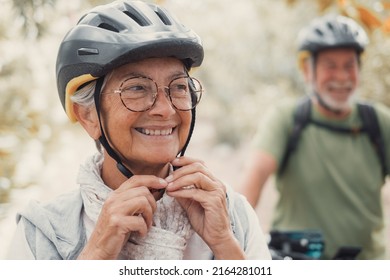 Portrait Of One Old Woman Smiling And Enjoying Nature Outdoors Riding Bike With Her Husband Laughing. Headshot Of Mature Female With Glasses Feeling Healthy. Senior Putting On Helmet To Go Trip 