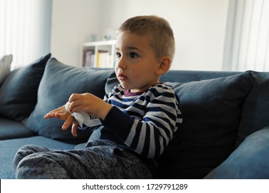 Portrait Of One Small Three Years Old Caucasian Boy Little Child Kid Sitting On The Sofa Bed At Home Holding Wet Wipe Napkin In Hand Wiping Mouth Face Clean And Disinfect Hands After Eating Side View