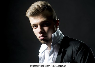 Portrait Of One Young Handsome Sensual Unshaven Bearded Man Model With Plush Lips Popped Unbuttoned Collar White Shirt Black Jacket Looking Forward In Studio On Black Background, Horizontal Picture