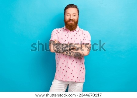 Portrait of optimistic friendly man with cool tattoo wear flamingo t-shirt standing hold arms crossed isolated on blue color background