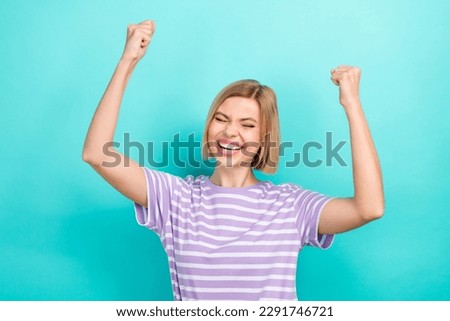 Portrait of optimistic woman with short haircut dressed stylish t-shirt raising fist up scream yeah isolated on teal color background