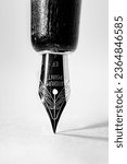 Portrait orientation image of a single fountain pen nib on a white paper background with two shadows cast by off camera flash