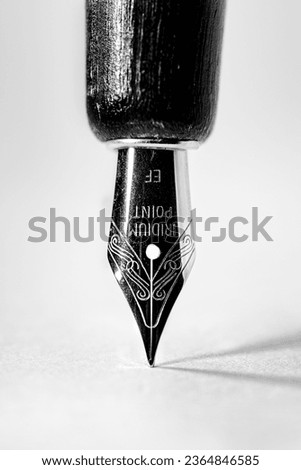 Portrait orientation image of a single fountain pen nib on a white paper background with two shadows cast by off camera flash