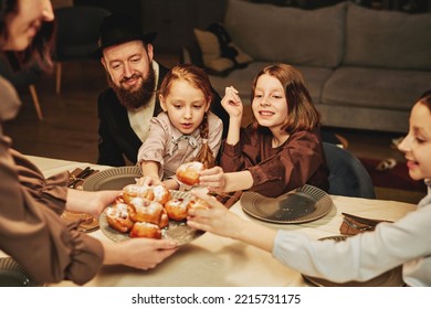 Portrait Of Orthodox Jewish Family With Children Enjoying Homemade Pastry At Dinner Table