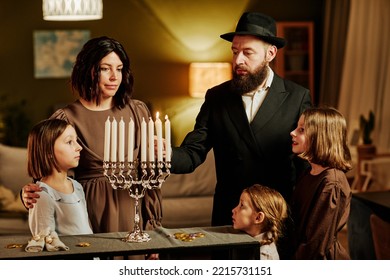 Portrait Of Orthodox Jewish Family Lighting Menorah Candle During Hanukkah Celebration At Home