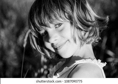 Portrait Outdoors At Sunset Of A Beautiful Kid Girl Among The Flowers. Black And White Photography. Innocence And Children Lifestyle. Summer