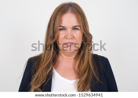 Portrait of outraged woman with oval face, blue eyes and long hair wearing formal clothes frowning her eyebrows being displeased with something. Scowling pretty female isolated over grey