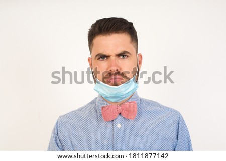 Portrait of outraged young man with oval face, blue eyes wearing medical mask frowning his eyebrows being displeased with something. Scowling pretty female isolated over grey.
