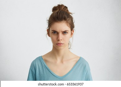 Portrait of outraged young woman with oval face, blue eyes and hair bun wearing blue casual sweater frowning her eyebrows being displeased with something. Scowling pretty female isolated over white - Shutterstock ID 653361937