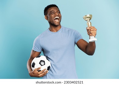 Portrait of overjoyed African American man, soccer player holding ball and trophy cup, celebration success isolated on blue background. Sport victory, winning competition concept - Powered by Shutterstock