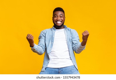 Portrait Of Overjoyed Black Man Celebrating Success With Clenched Fists And Euphoric Face Expression On Yellow Studio Background With Copy Space