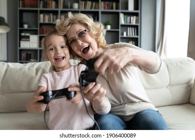 Portrait of overjoyed different female generations family playing video games at home. Happy little preschool child girl laughing, enjoying domestic hobby playtime with caring older grandmother. - Powered by Shutterstock