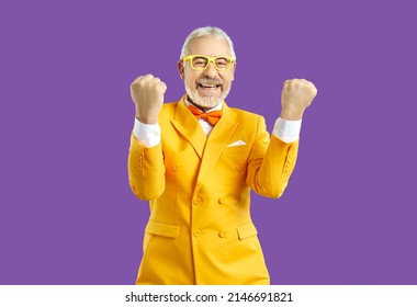 Portrait of overjoyed funny old man in suit and glasses isolated on purple studio background celebrate win. Smiling mature male make gesture enjoy lottery victory or good deal or offer.