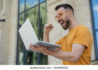 Portrait Of Overjoyed Online Lottery Winner Looking At Digital Screen Celebration Success. Sport Betting Concept. Excited Man Using Laptop Computer, Playing Video Games