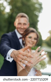 Portrait of overjoyed wedding couple standing outside, embracing hugging in park in summer, stretching hands forward, showing golden engagement rings. Relationship, love. Selective focus, vertical. - Shutterstock ID 2207715209