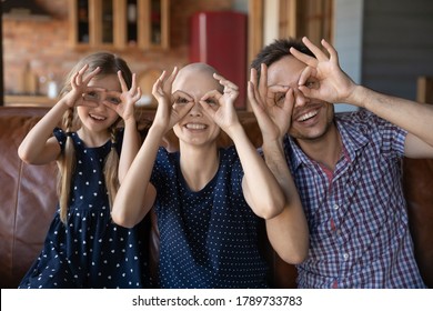 Portrait Of Overjoyed Young Family With Little Kid With Sick Cancer Patient Mother Make Funny Faces Relax At Home Together, Happy Man Support Ill Hairless Wife Feel Playful With Small Daughter Child